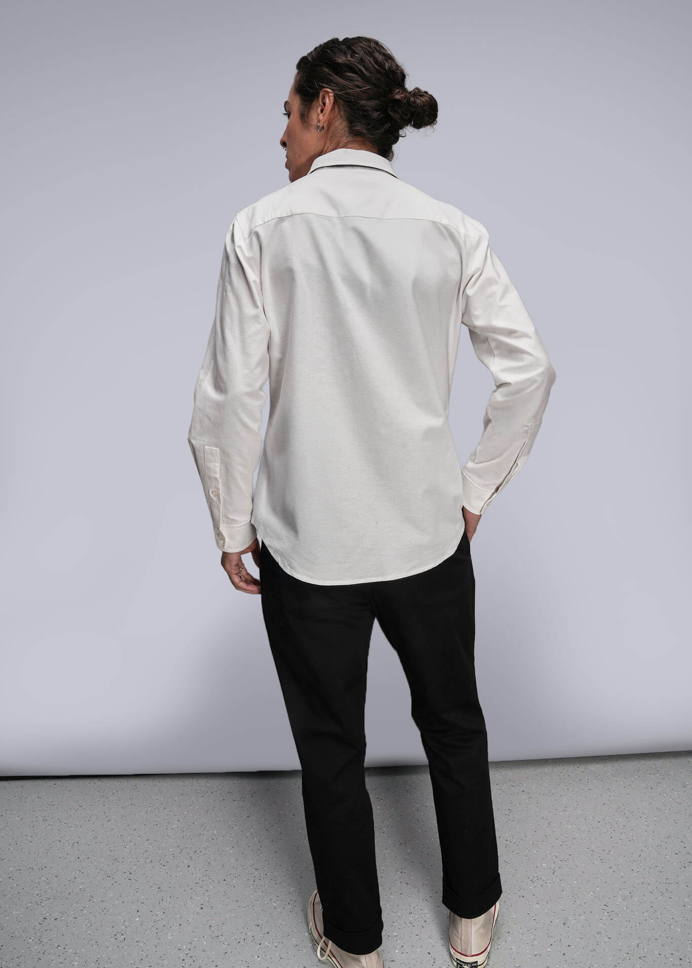 S=Person wearing a light-colored shirt and black pants against a plain background