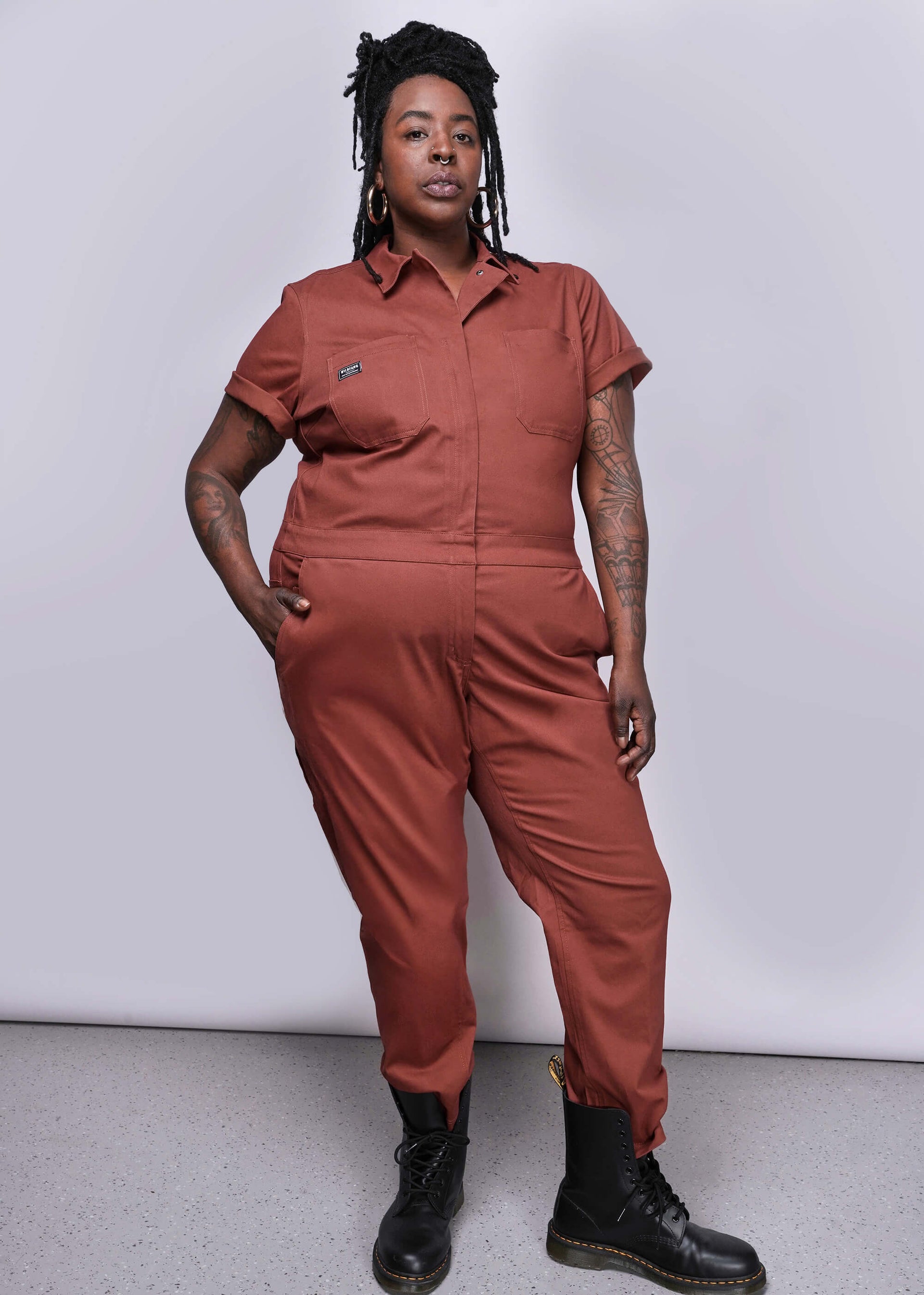 1X=Person wearing a cinnamon colored jumpsuit against a white background