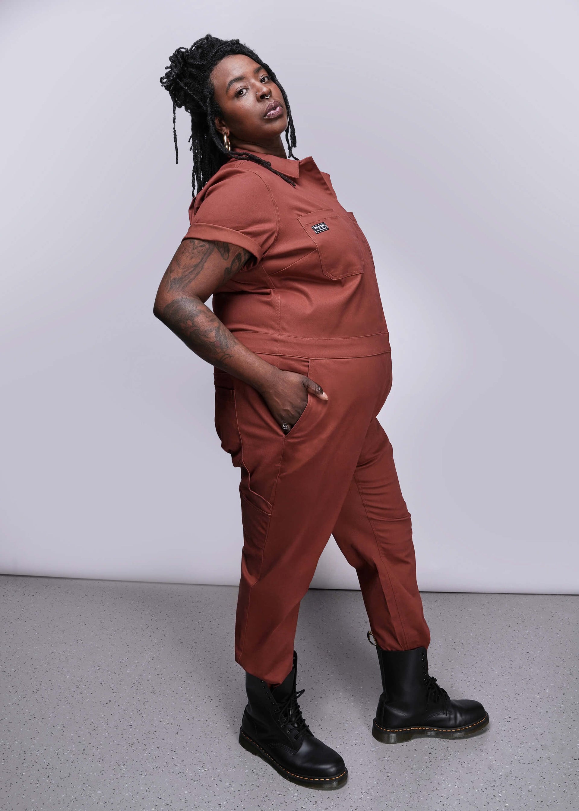 1X=Person wearing a dark orange jumpsuit with black boots against a white background