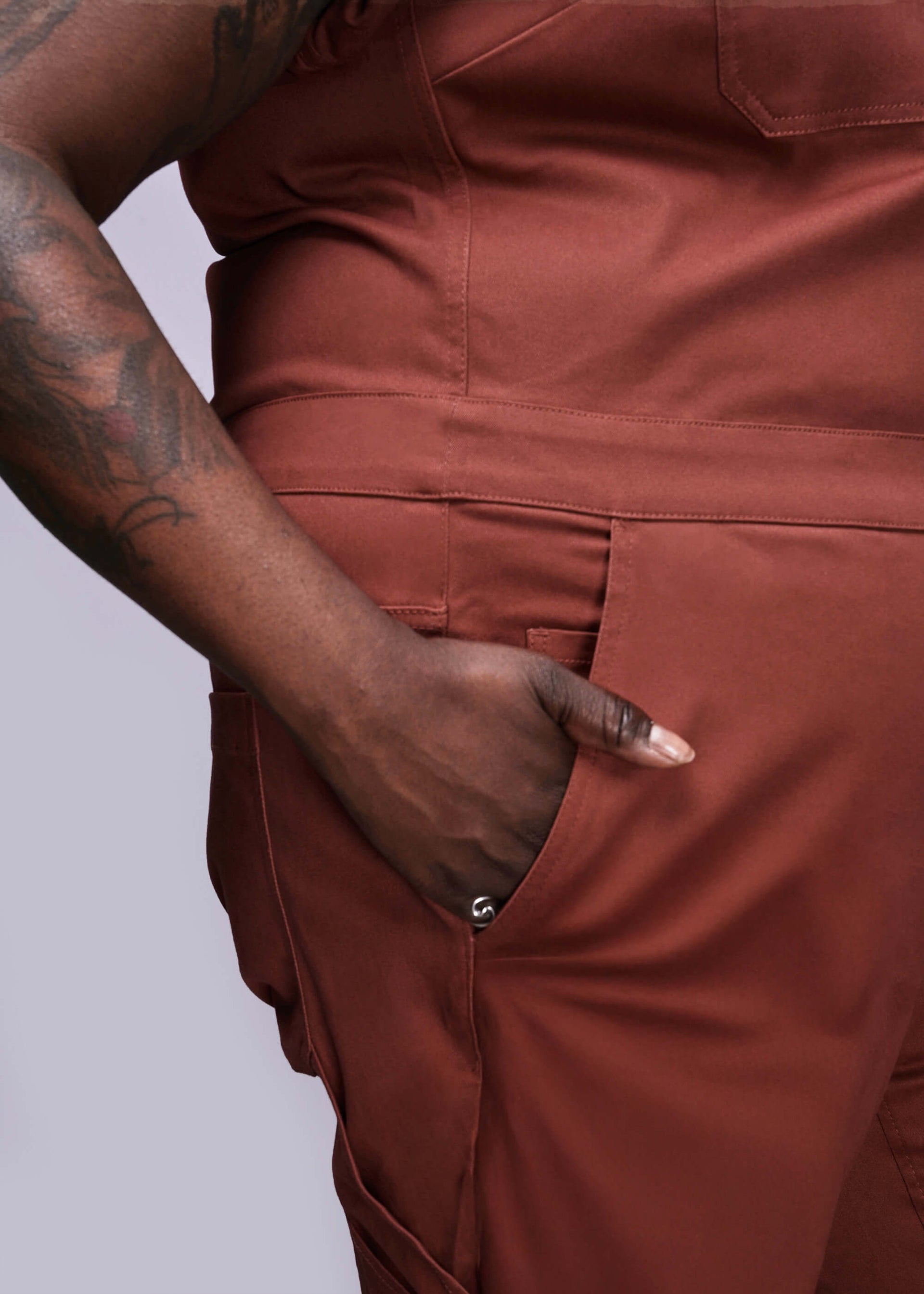 1X=Close up of dark orange jumpsuit worn by a person with tattoos on a plain background