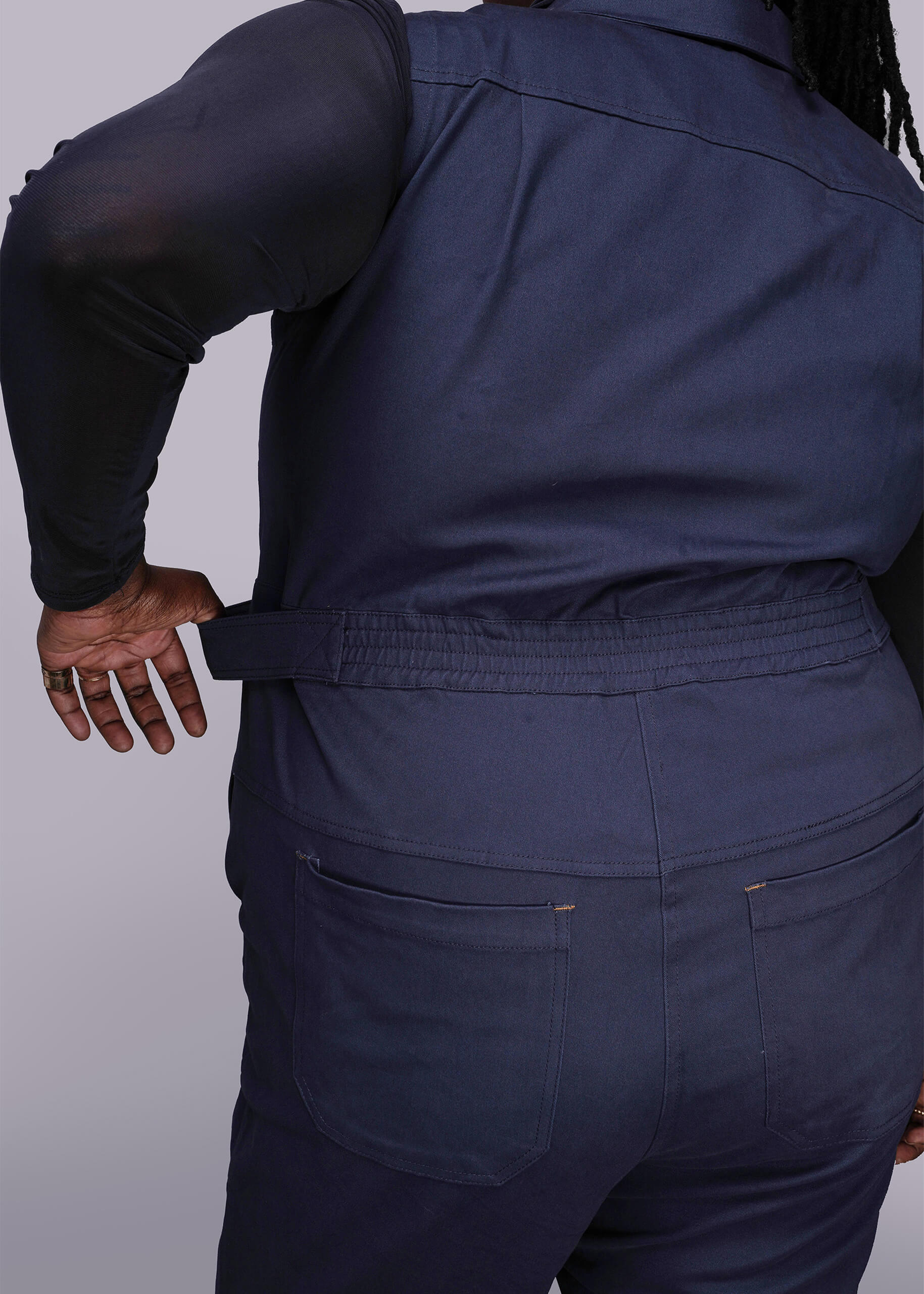 1X=Back of person wearing a navy blue jumpsuit holding waistband on a plain background