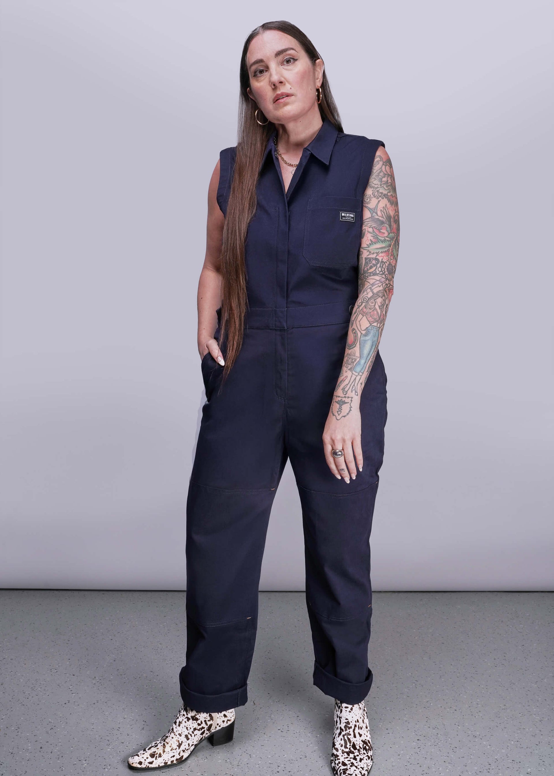 S=Woman wearing a navy blue sleeveless jumpsuit on a plain background