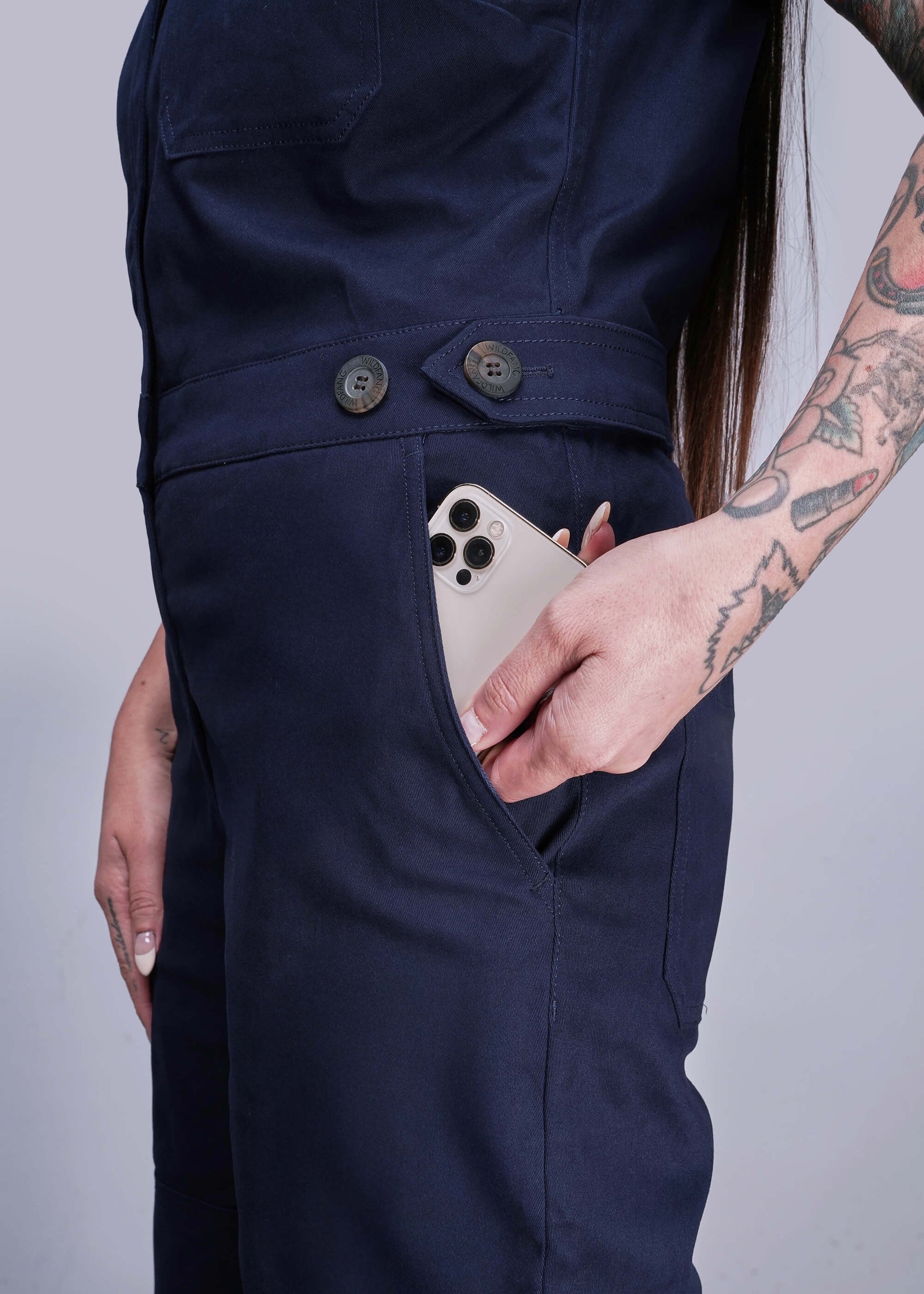 S=Person wearing navy blue pants with a phone in the pocket against a plain background
