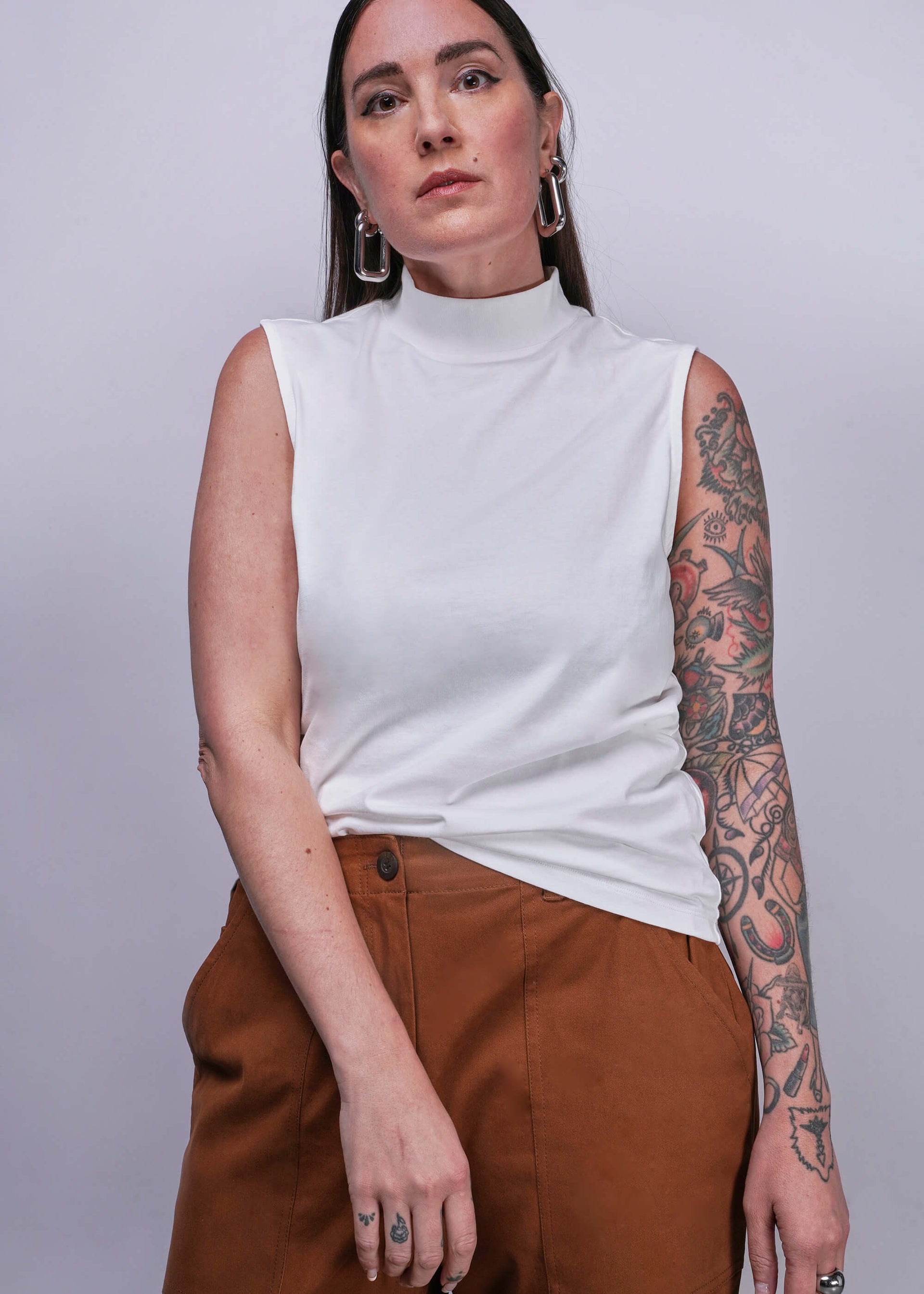S=Woman wearing a white sleeveless top and brown pants against a plain background