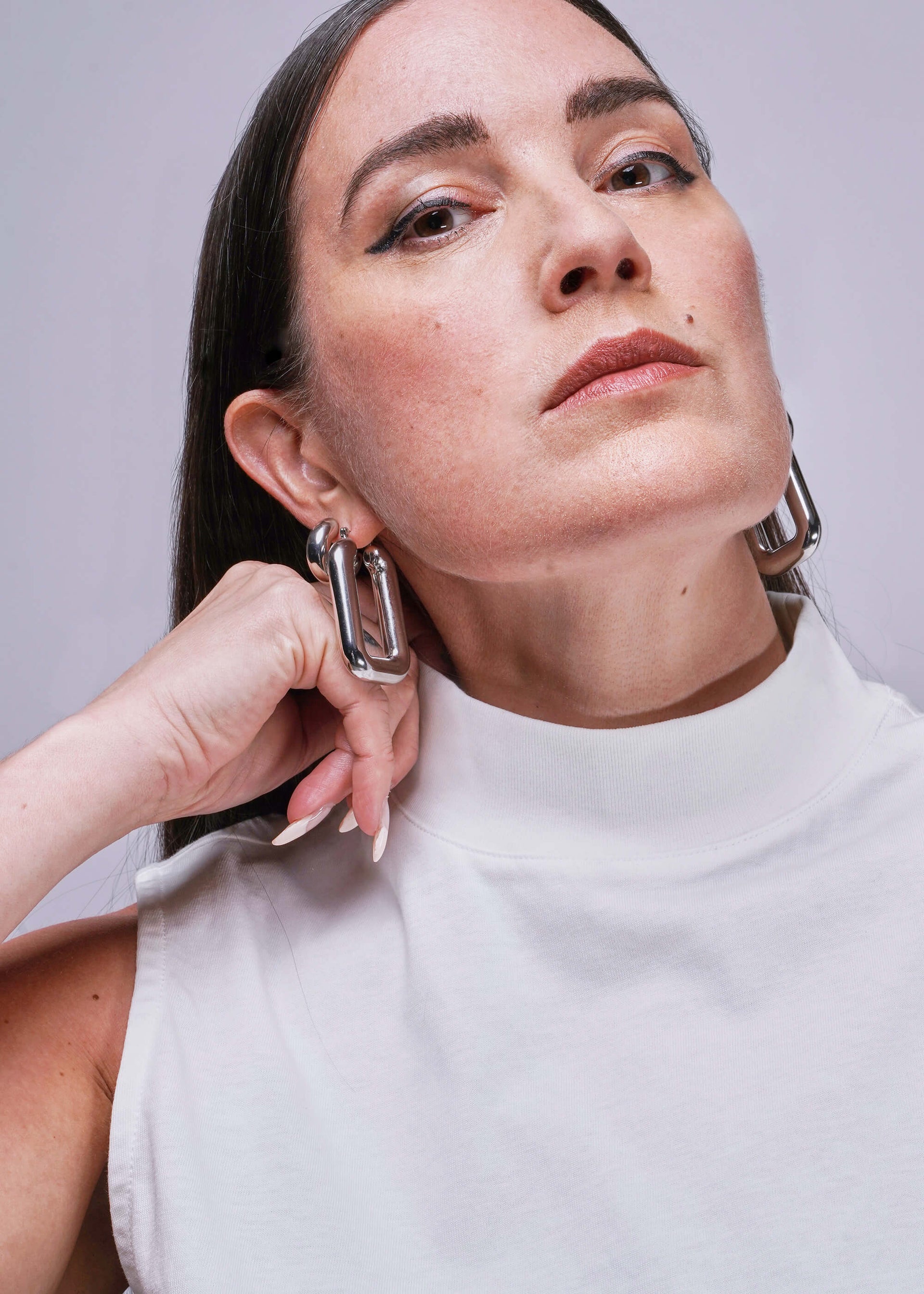 S=Woman wearing large hoop earrings shows collar of white tank top against a plain background