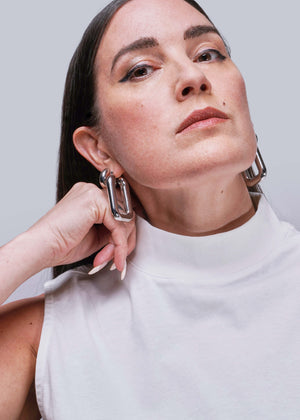 S=Woman wearing large hoop earrings shows collar of white tank top against a plain background