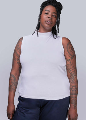 1X=Person wearing a white sleeveless top and dark pants against a plain background