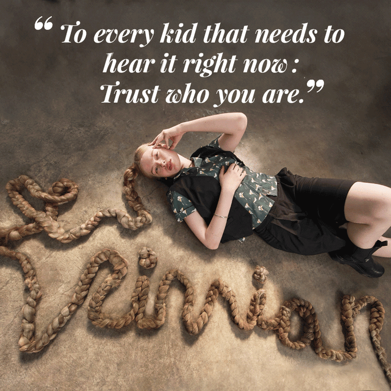 Vivian Wilson lays on floor with one leg crossed over the other, her hair is braided and is styled very long so that it spells out VIVIAN on the floor in cursive on front of her. She's wearing The Empower Vest in black, The Everyday Camp Button Up, and The Empower Wide Leg Short in Black. Text overlay on top of image is a quote from Vivian. It reads "To every kid that needs to hear it right now: trust who you are."