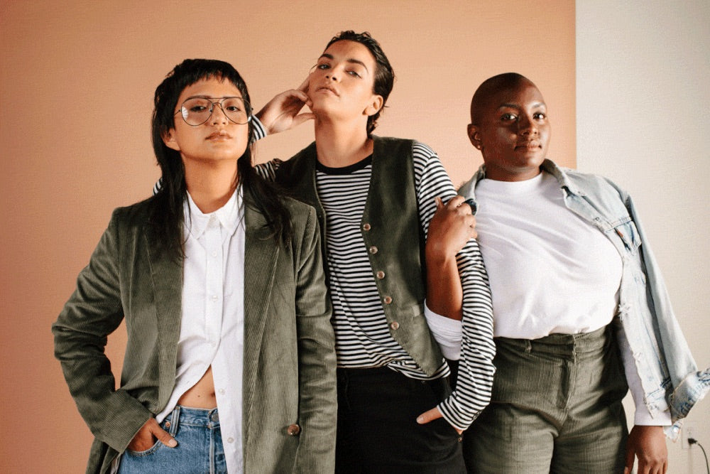 Three models wearing Wildfang clothing stand in front of two toned orange and white backdrop.