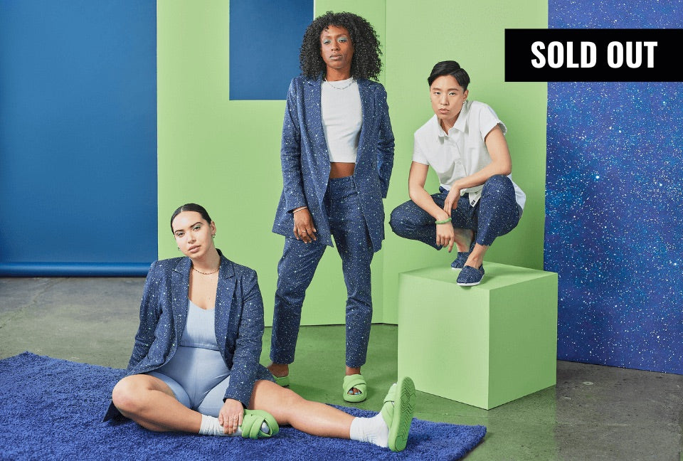 Three models, one sitting on blue rug, one standing, and one crouching on top of a green platform, look at camera while wearing pieces from the Toms x Wildfang collection. The background is lime green and blue. There is a banner in the top right corner that reads SOLD OUT.