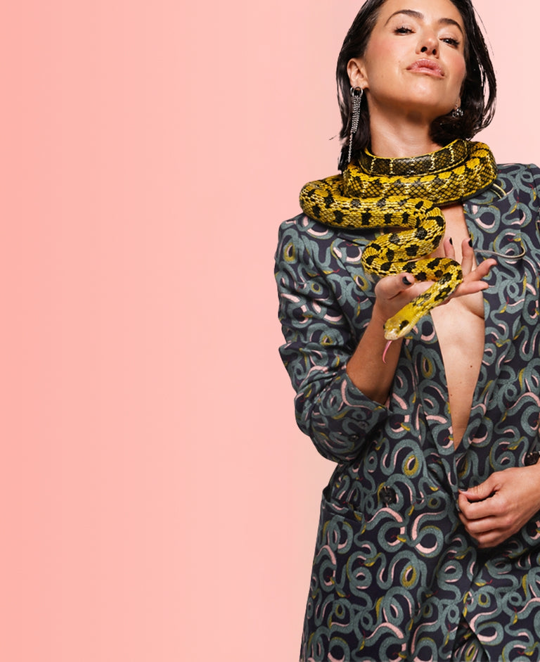 On peach colored background, Parvati Shallow wears the Serpentine Suit with yellow snake around her neck