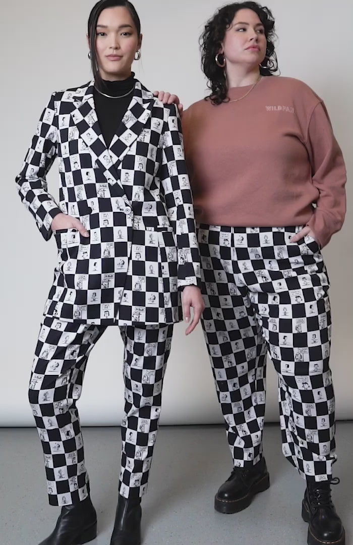 Video of two models in studio showcasing  the PEANUTS X WILDFANG slim crop pant. Shows close up of side and back pockets, bottom hem, belt loop, and custom black and white checkered print featuring Peanuts characters.