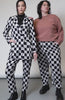 Video of two models in studio showcasing  the PEANUTS X WILDFANG slim crop pant. Shows close up of side and back pockets, bottom hem, belt loop, and custom black and white checkered print featuring Peanuts characters.