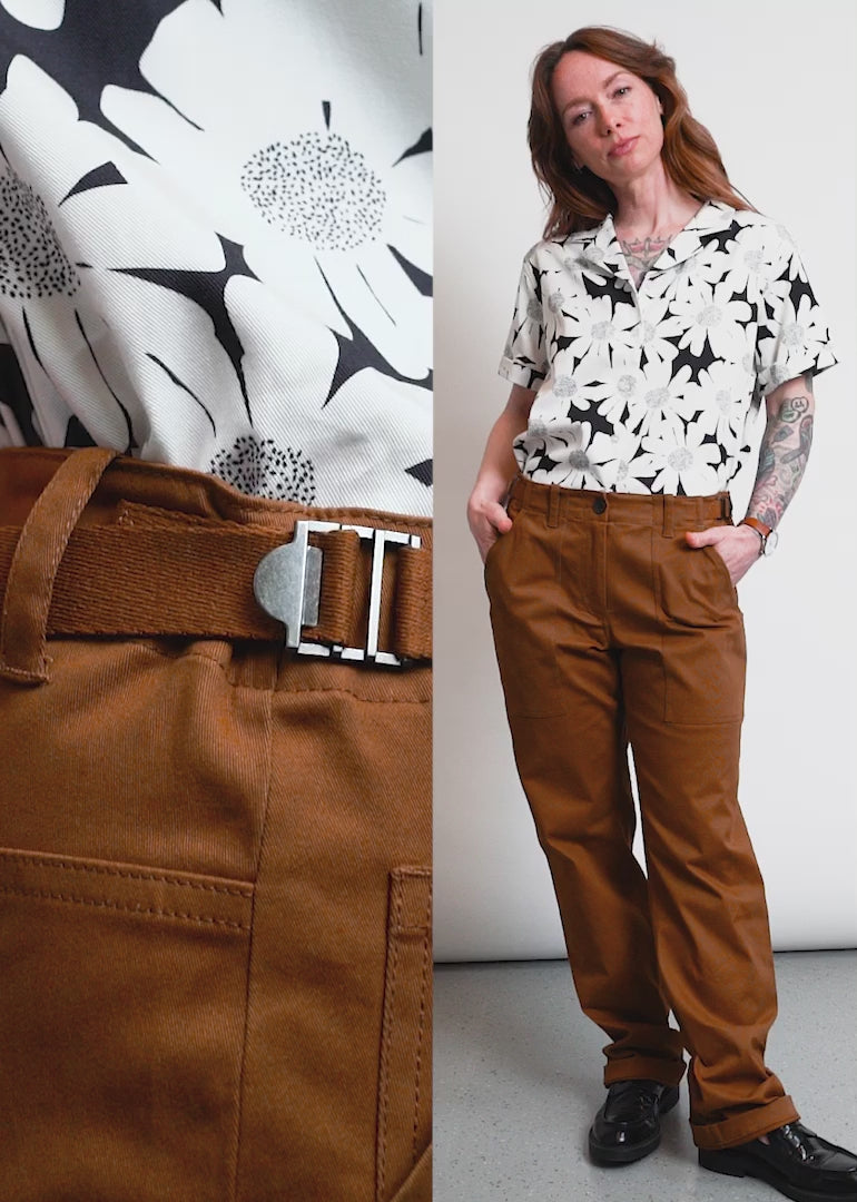 Video shows two models of different sizes wearing The Essential Utility Pant in Walnut. Close up shots show back and side pockets, the adjustable waist, and how the pant moves when the model squats. The video ends with a split screen side by side of the two models to show how it fits in different sizes.