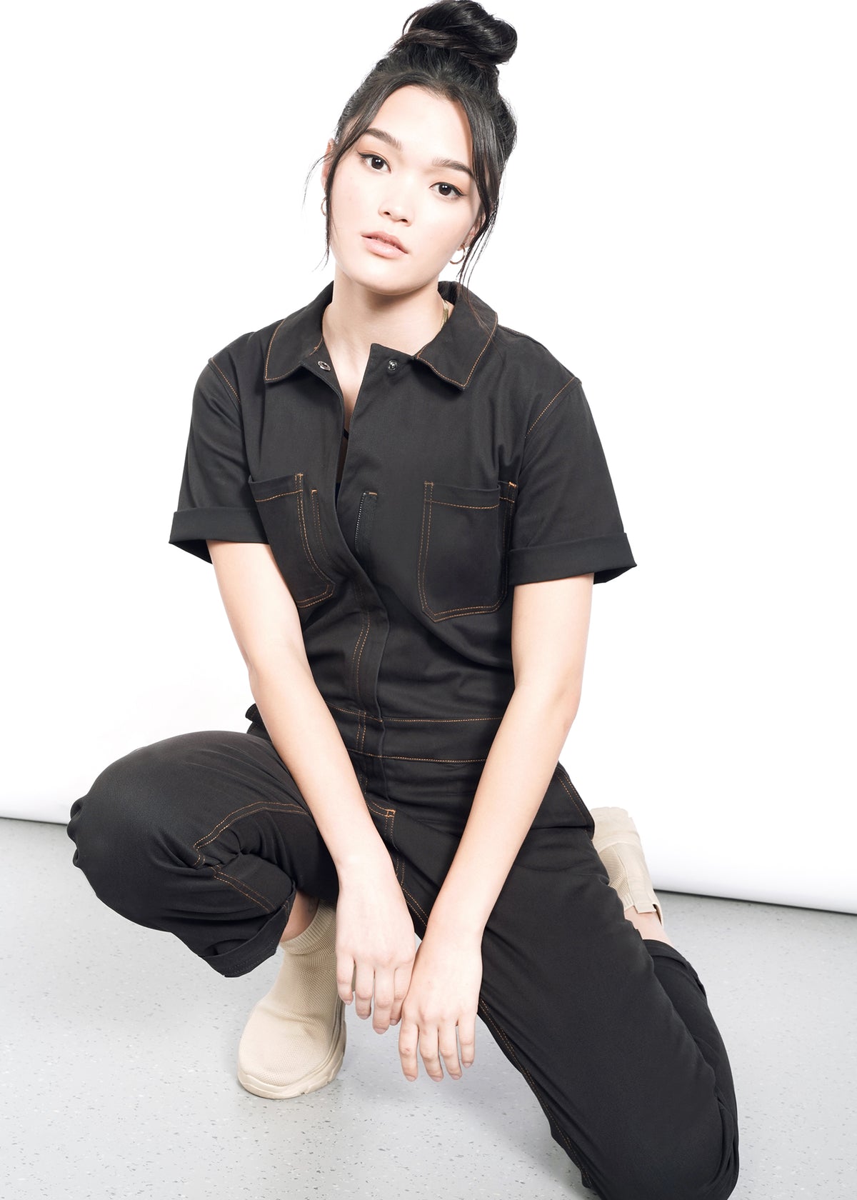 model wearing black cotton stretch coverall jumpsuit boiler suit short sleeve with brown spice colored pop stitching
