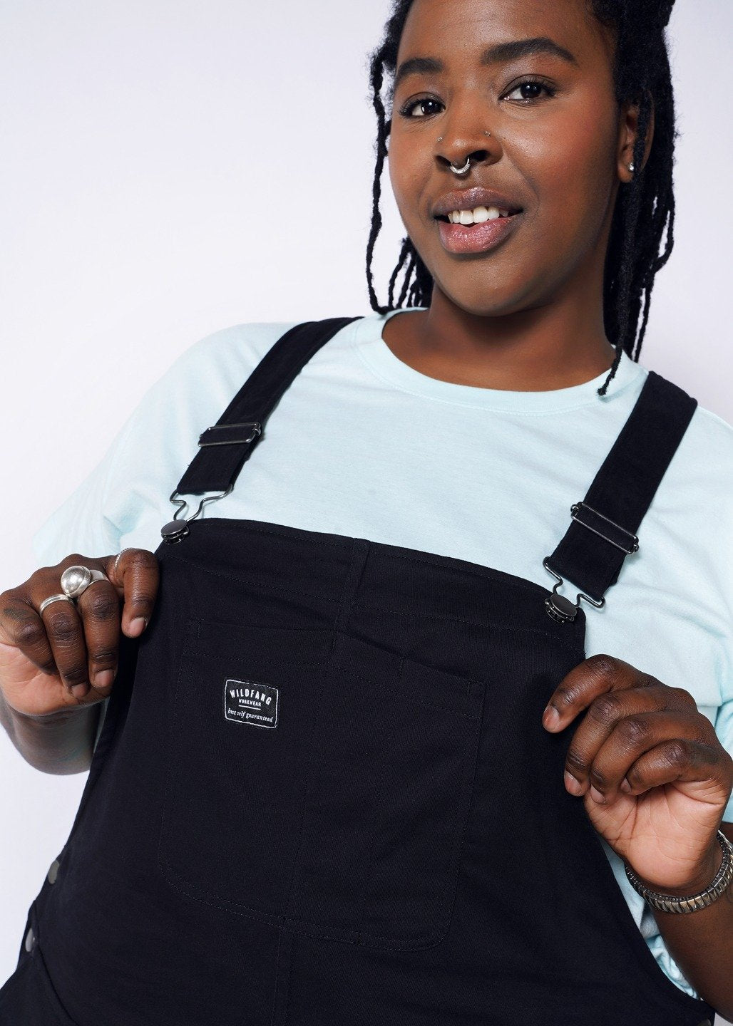 Model wearing black overalls with metal hardware in size XXL, with an blue tee underneath, holding front bib