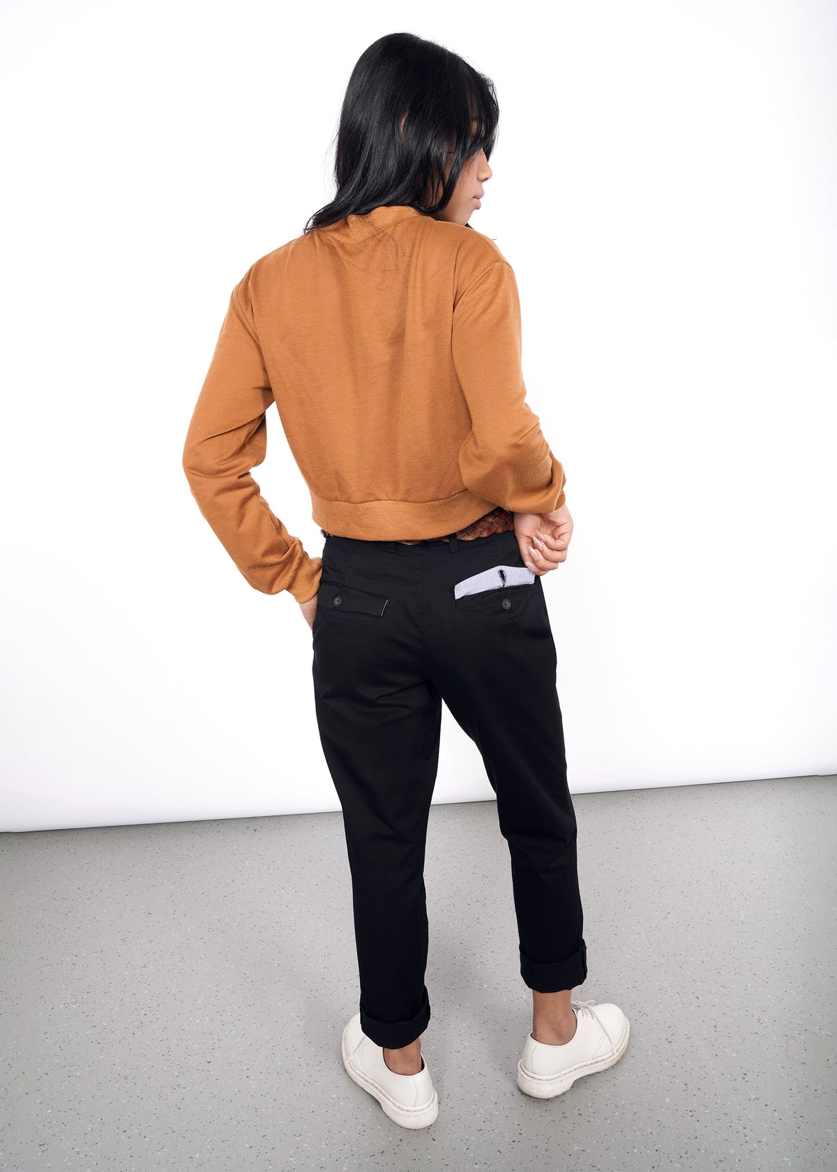 Back view of model wearing black essential trouser in size 2, lifting one pocket open to display interior lining