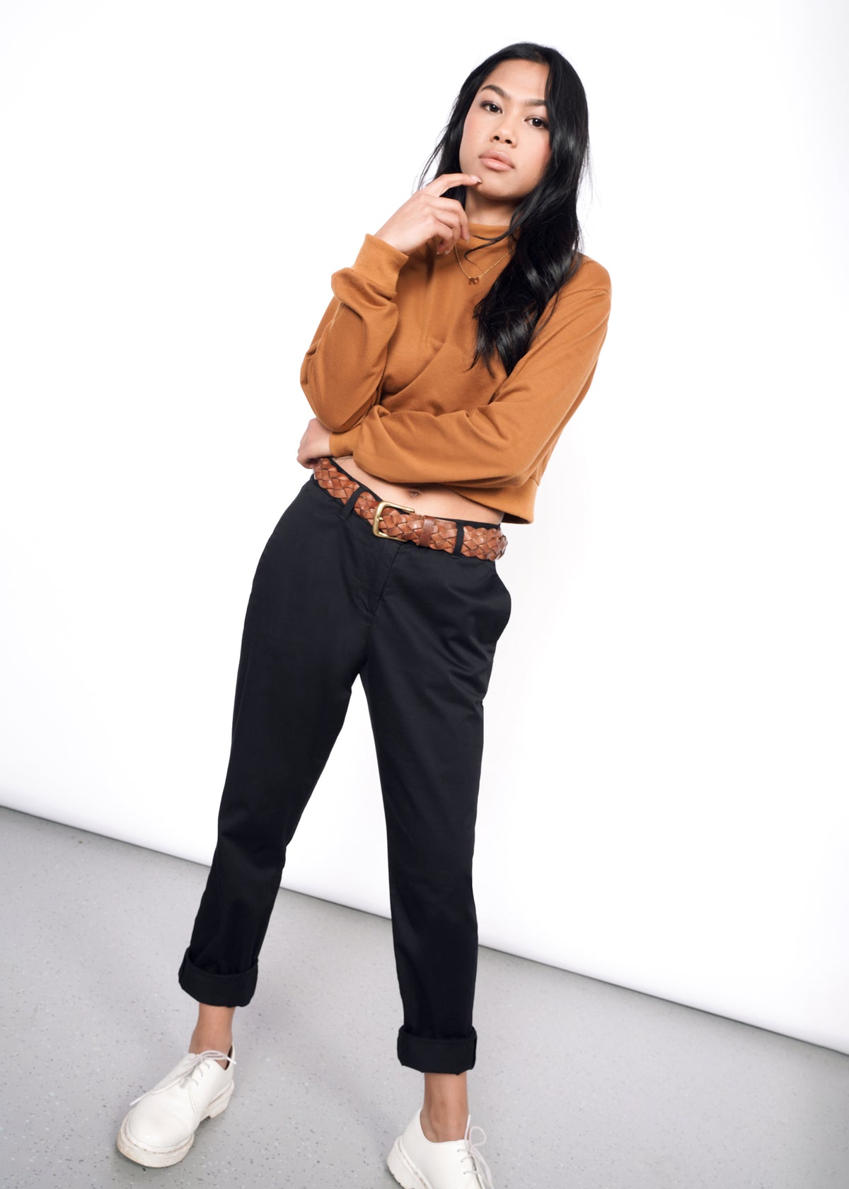 Model wearing black essential trouser in size two, styled with brown belt, burnt orange top, and white shoes
